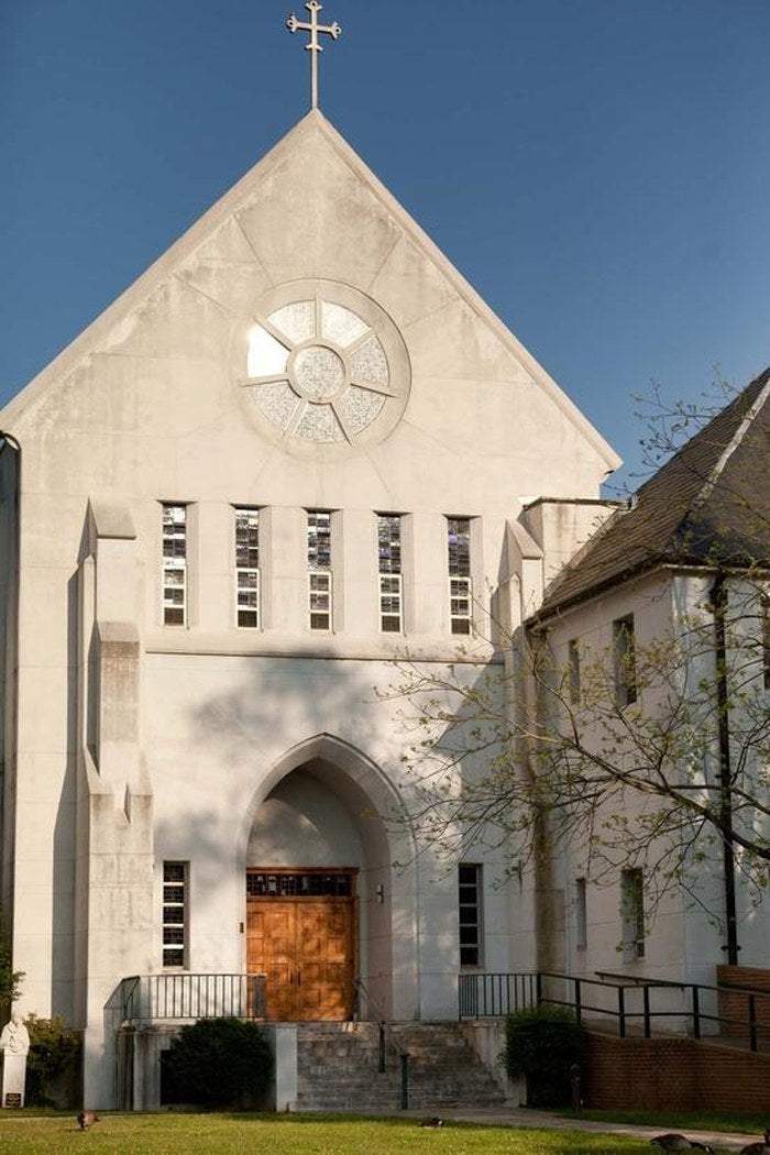 The Abbey Church at the Monastery of the Holy Spirit — a pale concrete gable with a round stained-glass window above timber doors, under a clear sky.