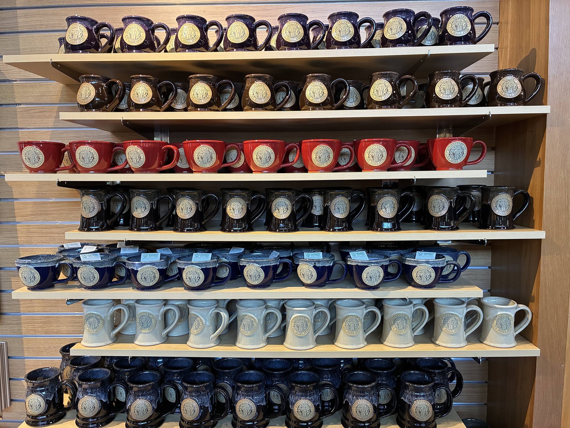 Rows of monastery mugs in blue, red and grey on the Abbey Store shelves.