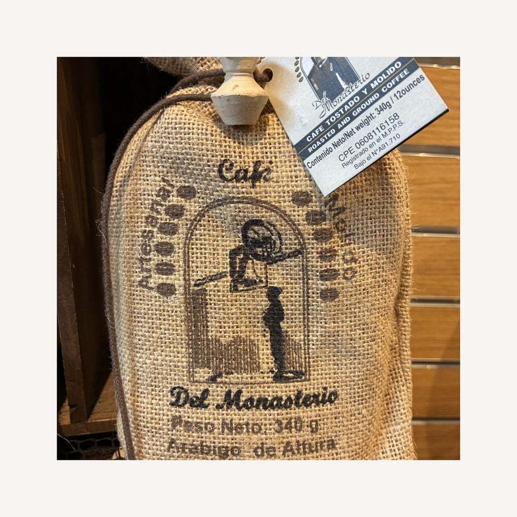 A burlap sack of Cafe del Monasterio ground coffee, stamped with the monastery emblem of a monk at an arched doorway, 340 g