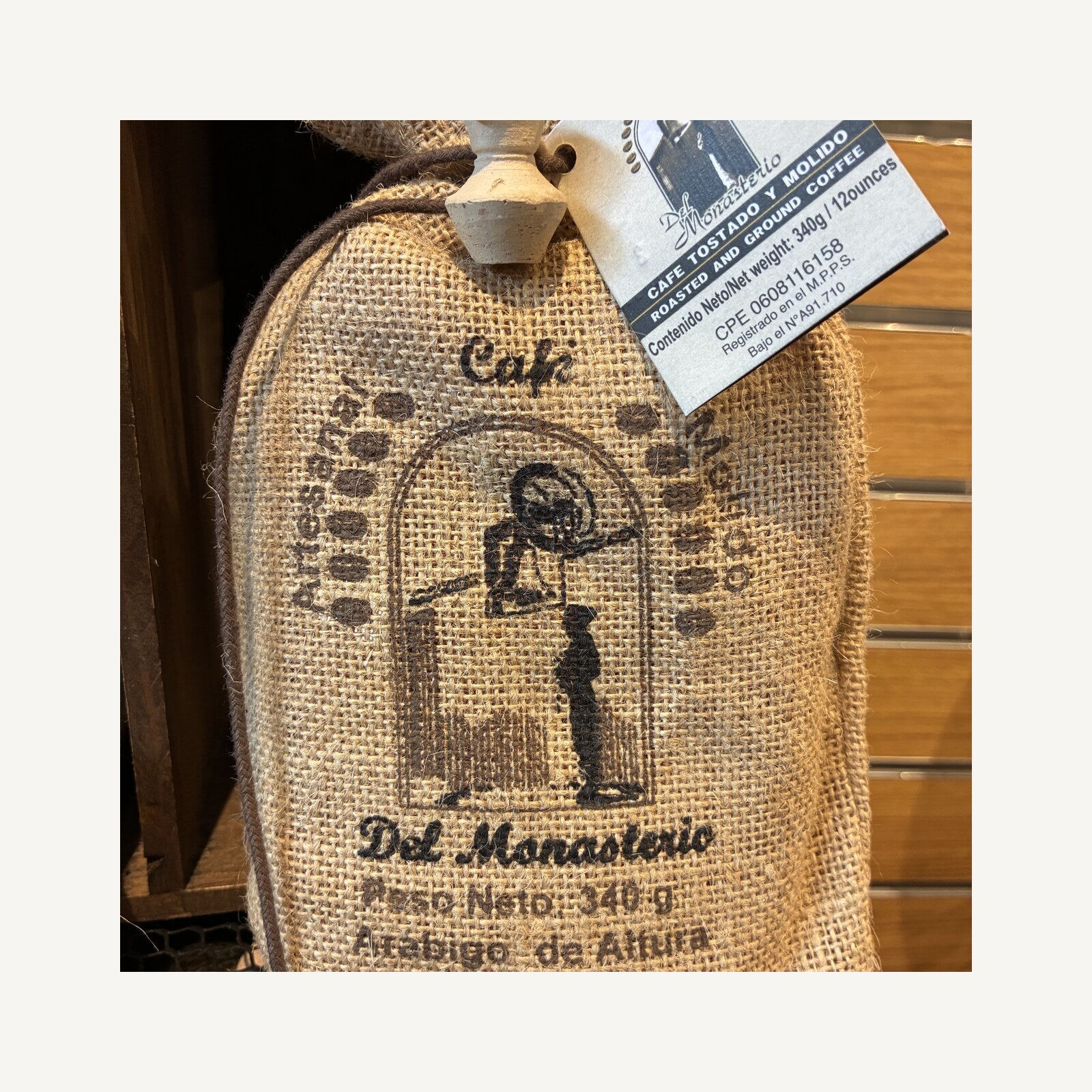 A burlap sack of Cafe del Monasterio ground coffee, stamped with the monastery emblem of a monk at an arched doorway, 340 g